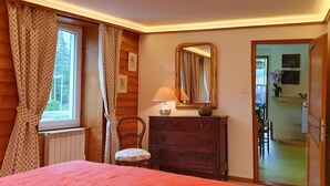 Une chambre à coucher avec un lit, des murs en bois, une commode, une chaise, une fenêtre avec des rideaux et un miroir.