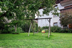 Een tuin met een schommel, een gazon en een gebouw op de achtergrond.