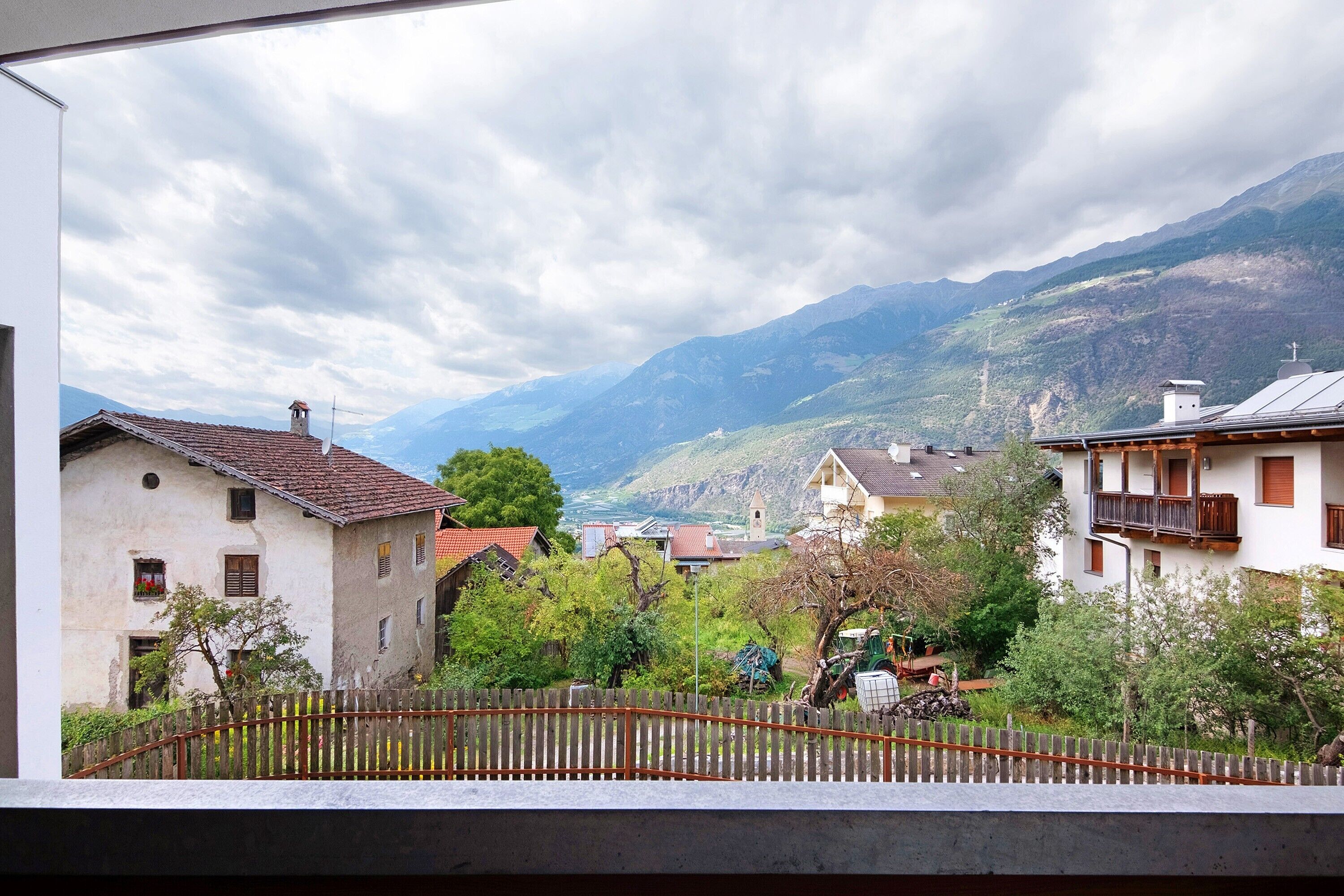 A mountainous landscape with traditional buildings, a wooden fence, and a clear sky.