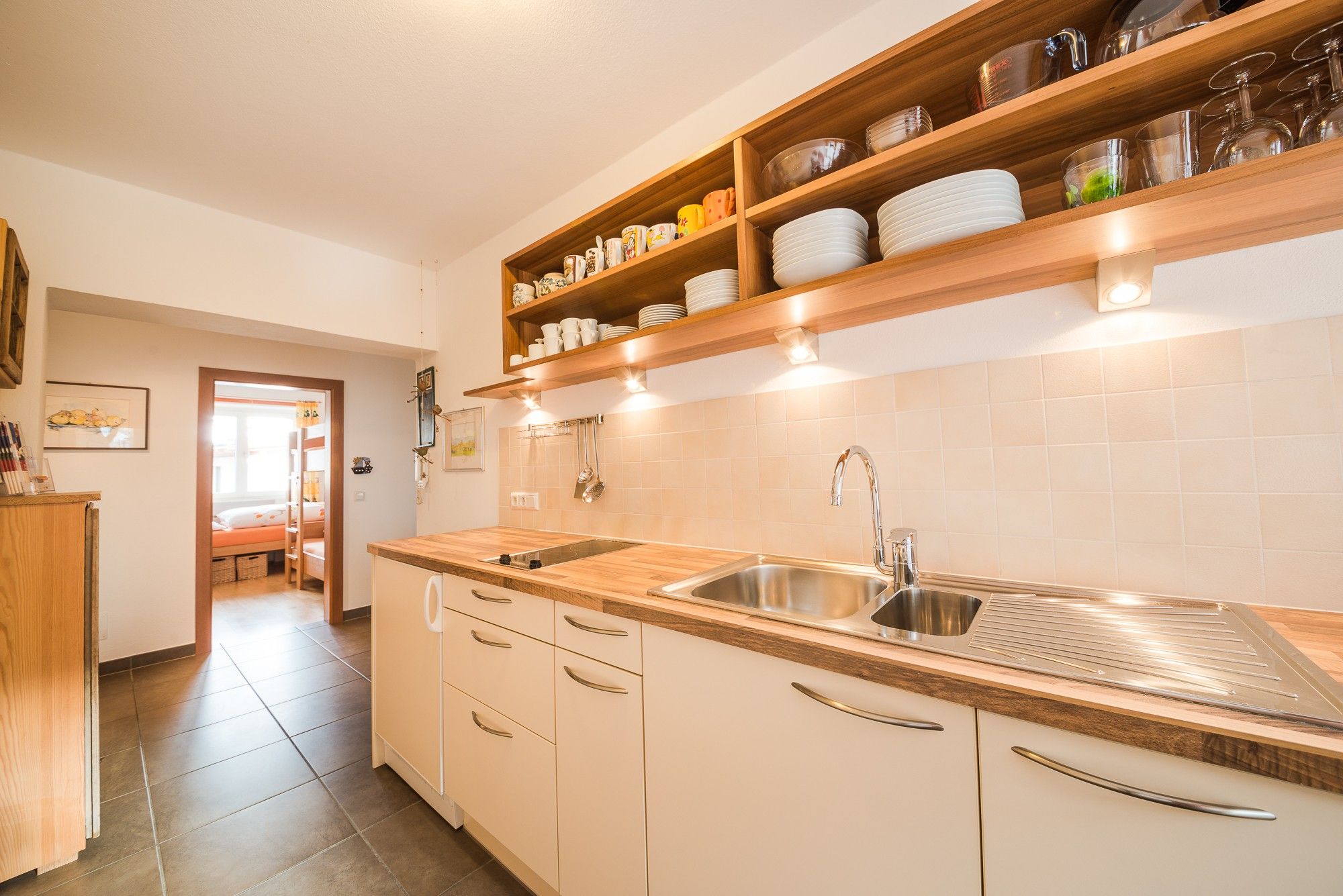 A modern kitchen with a wooden countertop, stainless steel sink, and built-in shelves above the counter.