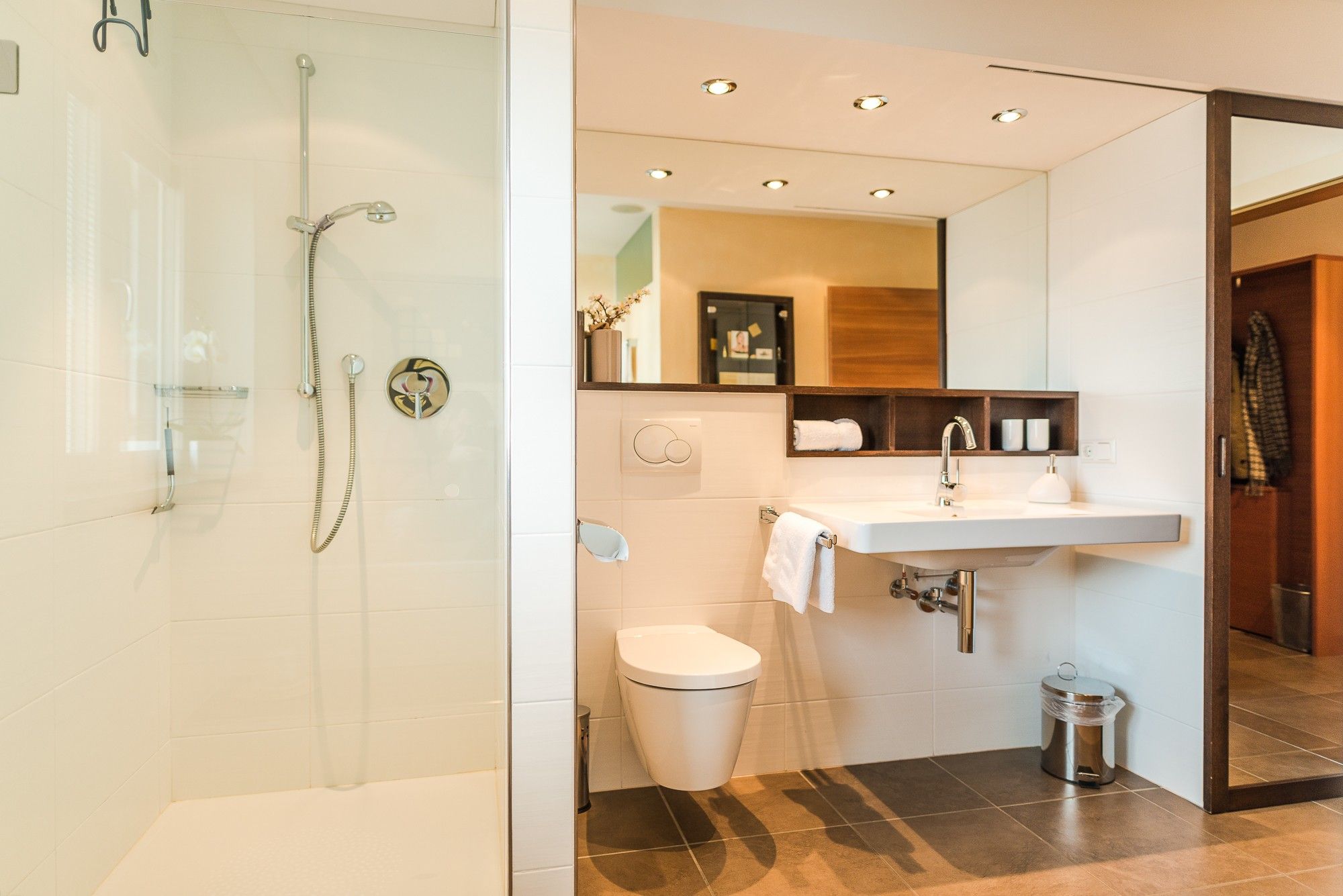 Ein modernes Badezimmer mit einer gläsernen Duschkabine, einem weißen Waschbecken mit Spiegel darüber und einer Toilette.