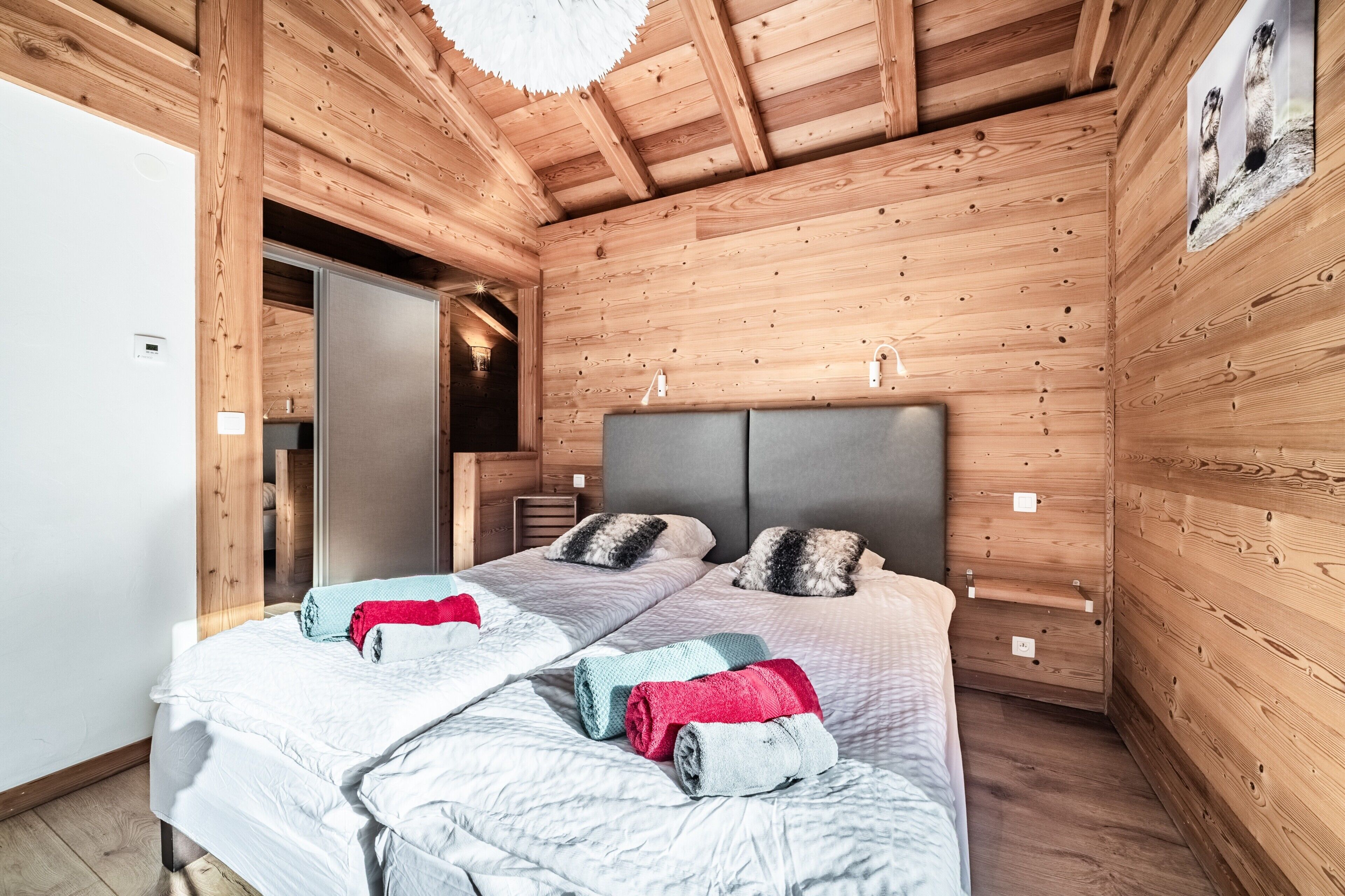 A wooden cabin bedroom with two beds, a wardrobe, and a door leading to another room.