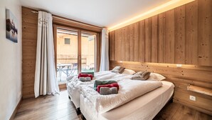 A bedroom with a wooden headboard, a large bed with multiple pillows, a window with curtains, and a wooden floor. - Chalet 'Heidi - Chatel' with Mountain View, Private Terrace and Wi-Fi (Châtel)