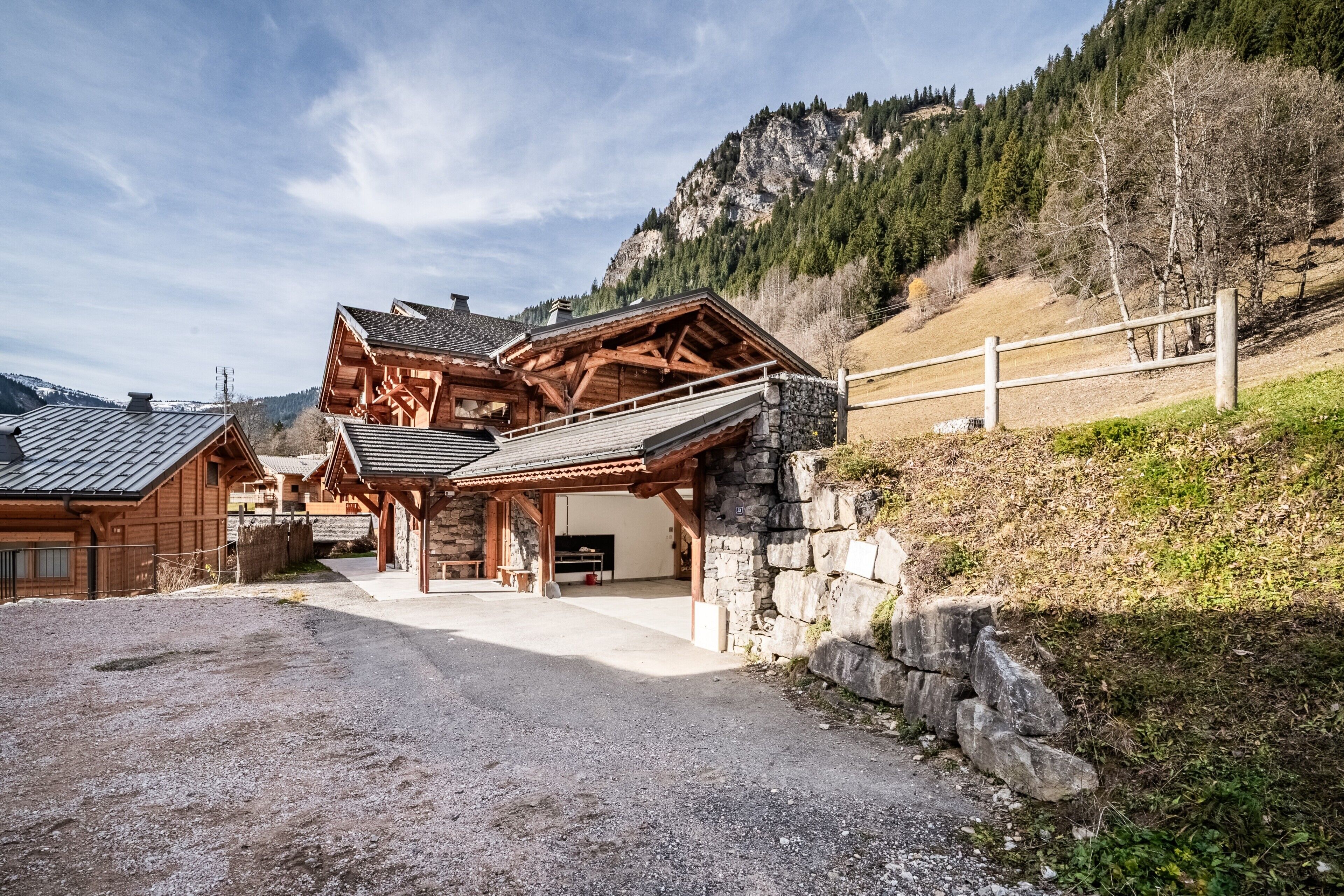A wooden lodge with a stone wall and a gravel driveway.