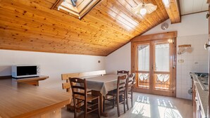 Un plafond en bois agrémenté de lucarnes, une table à manger avec des chaises, un coin cuisine et un banc intégré.