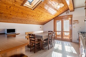 Techo de madera con tragaluces, una mesa de comedor con sillas, una zona de cocina y un banco empotrado.