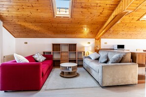Een moderne woonkamer met houten balken in het plafond, een rode bank, een grijze bank, een houten salontafel en inbouwplanken.
