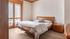 Une chambre à coucher avec un lit en bois, une table de chevet, une fenêtre avec des rideaux et un ventilateur de plafond.