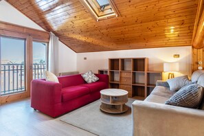 Een woonkamer met een rode bank, een beige bank, een houten salontafel en een boekenkast.
