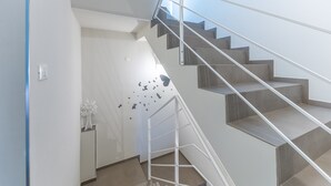 Een moderne trap met een metalen leuning, een witte muur met een decoratieve boom, en een muursticker met vlinders.