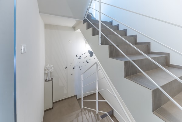 A modern staircase with a metal railing, a white wall with a decorative tree, and a wall decal with butterflies.