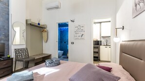 Een slaapkamer met een bed, een stoel, een bureau, een spiegel en een badkamer zichtbaar door een geopende deur.