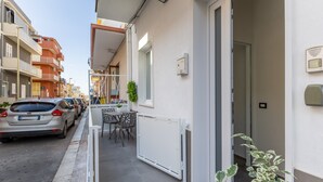 Een smalle straat met geparkeerde auto's, een balkon met een tafel en stoelen, en een gebouw met een witte gevel.