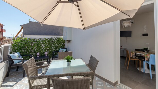 A balcony with a table and chairs, a large umbrella, and a wall with plants. - Holiday Home "La Dimora della Luna" with Sea View, Terrace and Wi-Fi (Pozzallo)