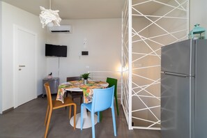 Une cuisine compacte comprenant une table à manger, des chaises, un réfrigérateur et un téléviseur fixé au mur.