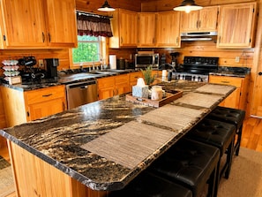 A kitchen with wooden cabinets, a granite countertop, stainless steel appliances, and a central island with stools.