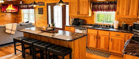 A cabin-style kitchen with wooden cabinets, a central island with stools, and a fireplace.