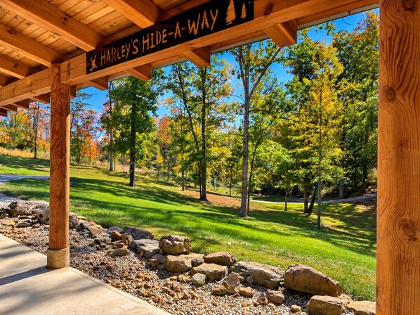 Una pérgola de madera con un letrero que dice 'HARLEY'S HIDE-A-WAY' y vistas de un parque con árboles y un sendero.