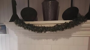 Un caminetto con mensola decorata da una ghirlanda, una sedia e uno scaffale con vasi.