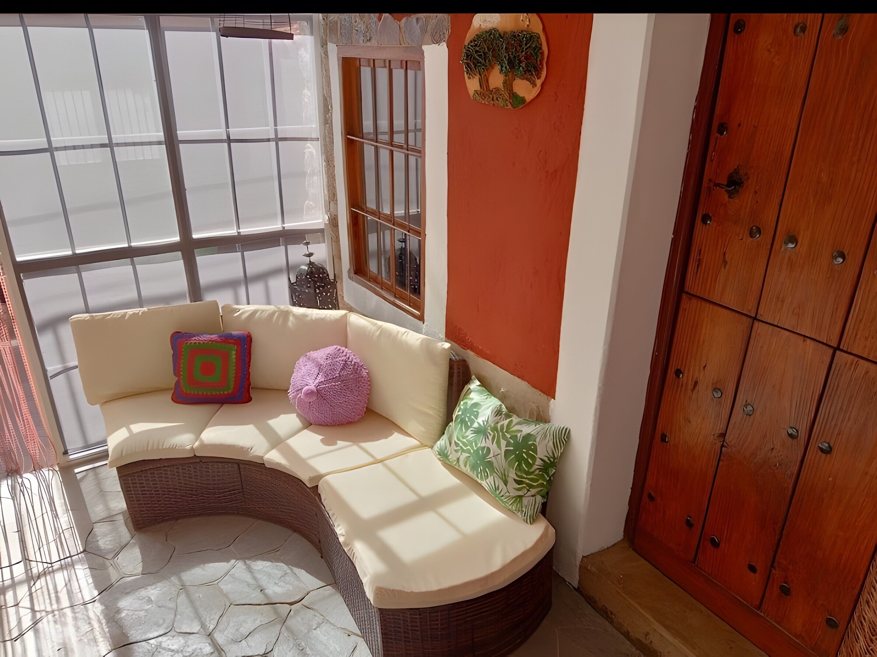 Una habitación de esquina con un sofá de mimbre, una ventana con rejas, un armario de madera y un adorno en la pared.