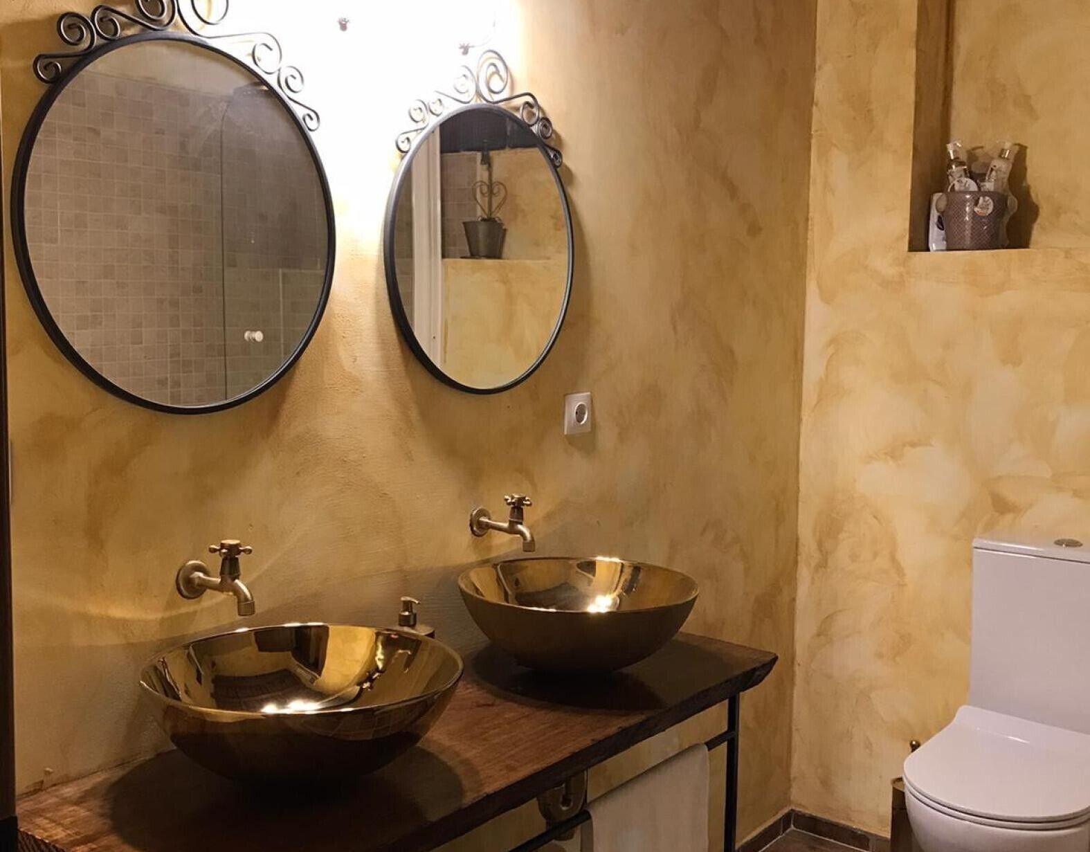 A bathroom with two round mirrors, a double sink with a bowl design, and a toilet.