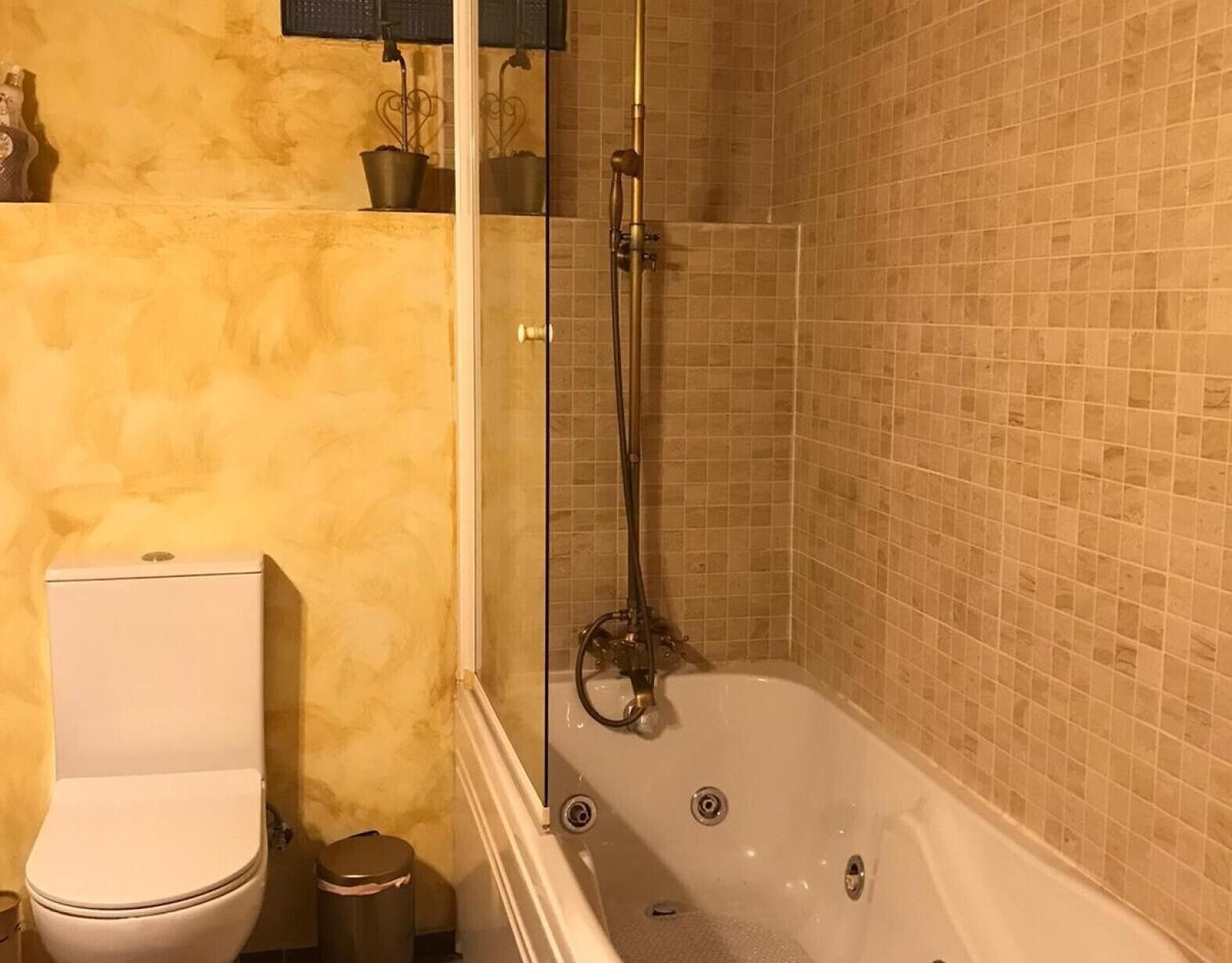 Un baño con inodoro, un cubo de basura, ducha con puerta de cristal y bañera.