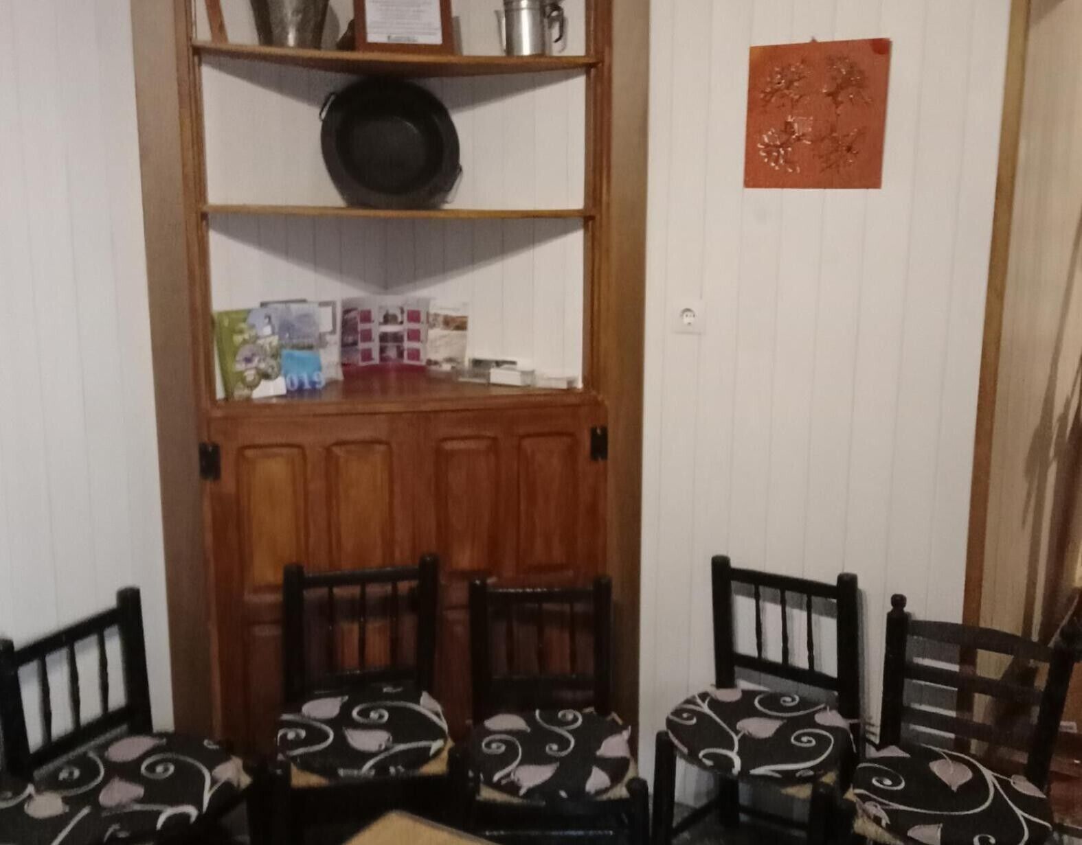 Un comedor con un mueble de madera, una estantería con un plato negro y sillas estampadas.