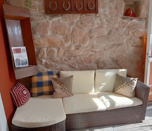 Un canapé en osier avec des coussins, un coussin à carreaux et un coussin rouge posés sur un sol carrelé.