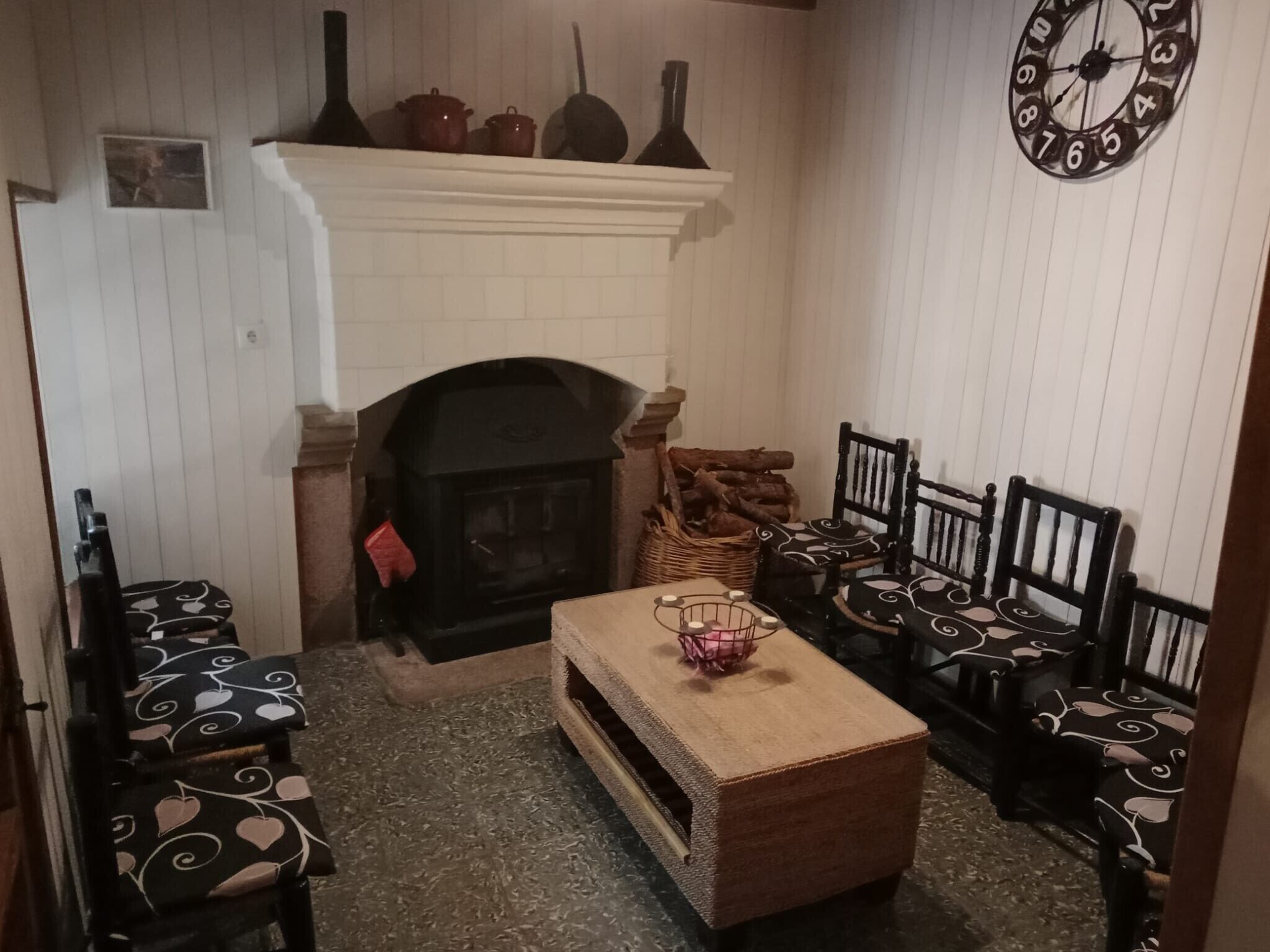 Una sala de estar acogedora con chimenea, sillones estampados, una mesa de centro y un reloj en la pared.