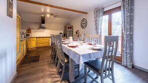 Un comedor con una mesa dispuesta para cuatro, sillas de madera, un reloj en la pared y una ventana con cortinas.