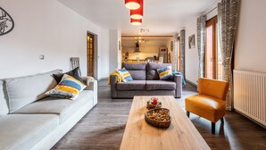 Una sala de estar moderna con un sofá, una mesa de centro y una silla. Se observa una cocina al fondo.