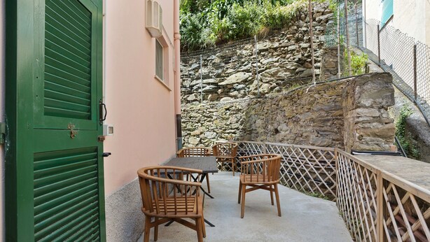 Un patio con sillas y una mesa de madera, una puerta verde y un muro de piedra al fondo.