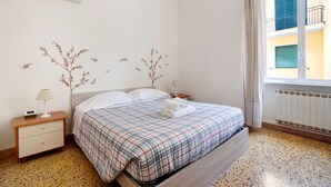 Un dormitorio con cama, mesita de noche, aire acondicionado de pared, ventana con cortinas y radiador.