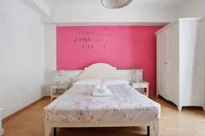 A bedroom with a bed, a nightstand, a wardrobe, and a pink wall with a motivational quote. - Room 'Camera Rosa' with Balcony, Wi-Fi and Air Conditioning (Riomaggiore)