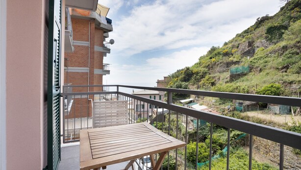 A balcony with a table, a view of a hillside, and a building with a brick facade. - Room 'Camera Rosa' with Balcony, Wi-Fi and Air Conditioning (Riomaggiore)