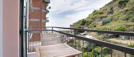 A balcony with a table, a view of a hillside, and a building with a brick facade.