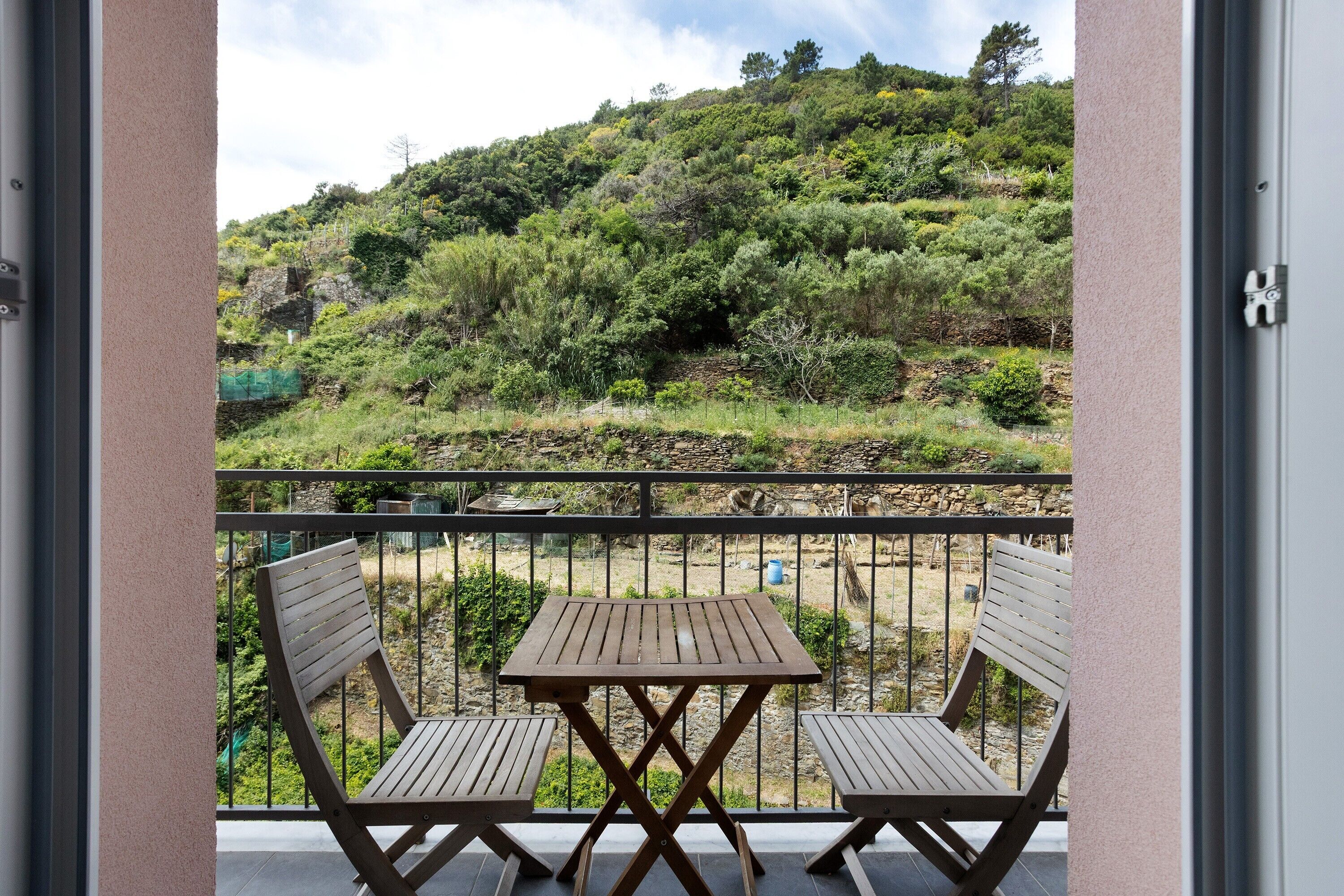 Ein Balkon mit zwei Holzstühlen und einem Tisch, mit Blick auf eine hügelige Landschaft mit dichter Vegetation.