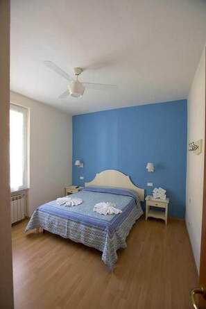 A bedroom with a bed, a ceiling fan, bedside lamps, and a window.