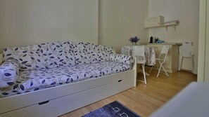 A small, single-room apartment with a sofa, a desk, and a chair.