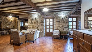 Ein rustikales Interieur mit Steinwänden, Holzbalken, Korbmöbeln und einem Kachelboden.
