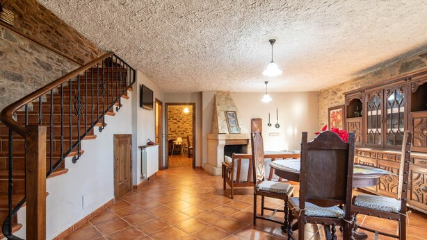 Ein geräumiger Raum mit einer Holztreppe, einer Essecke mit Tisch und Stühlen sowie einem Kamin aus Stein.
