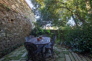 Un mur de pierre, une table ronde entourée de chaises et des plantes en pot, le tout dans un cadre de jardin.