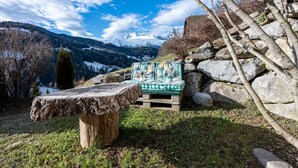 Un espacio de estar al aire libre rústico con una mesa de madera y un banco, rodeado de rocas y árboles, con vistas a un paisaje montañoso.