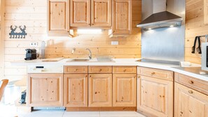 Interior de una cabaña de madera con cocina, que cuenta con armarios de madera, una campana extractora de acero inoxidable y un lavamanos.