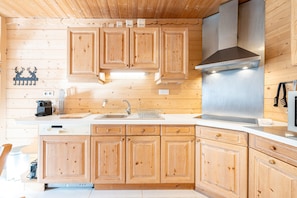 A wooden cabin interior with a kitchen featuring wooden cabinets, a stainless steel range hood, and a sink.