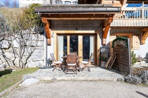 A wooden building with a stone patio, a wooden table with chairs, and a wooden fence.