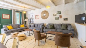 A living room with two grey sofas, a brown armchair, a wooden coffee table, and a television on a stand. - Gîte 'Le Cottage' with Shared Pool, Private Terrace and Wi-Fi (Saint-Romain-de-Benet)