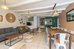 A modern living room with a sofa, coffee table, dining table, and chairs. There is a kitchen in the background. - Gîte 'Le Cottage' with Shared Pool, Private Terrace and Wi-Fi (Saint-Romain-de-Benet)