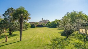 A grassy field with a building in the distance, surrounded by trees and shrubs. - Gîte 'Le Cottage' with Shared Pool, Private Terrace and Wi-Fi (Saint-Romain-de-Benet)