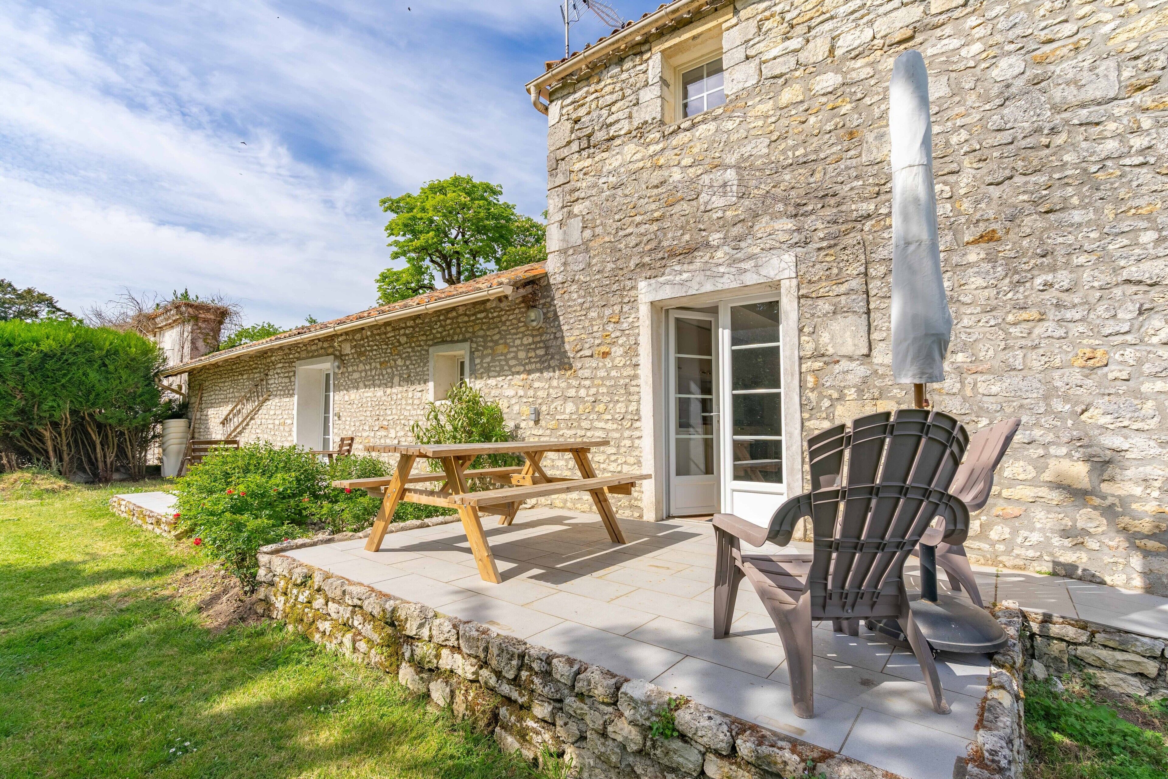 A stone building with a patio area, a wooden table, and a chair.